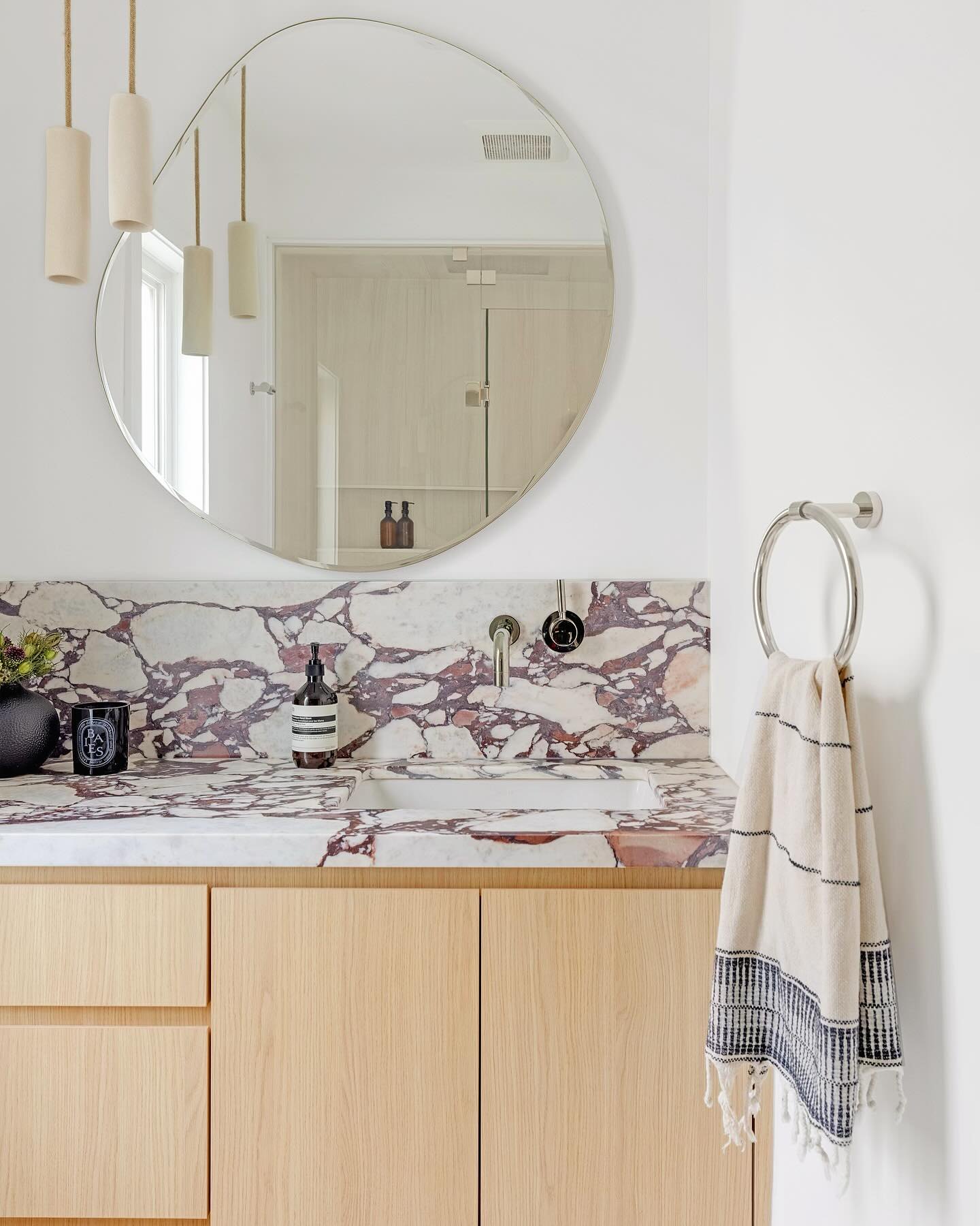 A bathroom clad in heavily veined Calacatta Viola marble with brass fittings