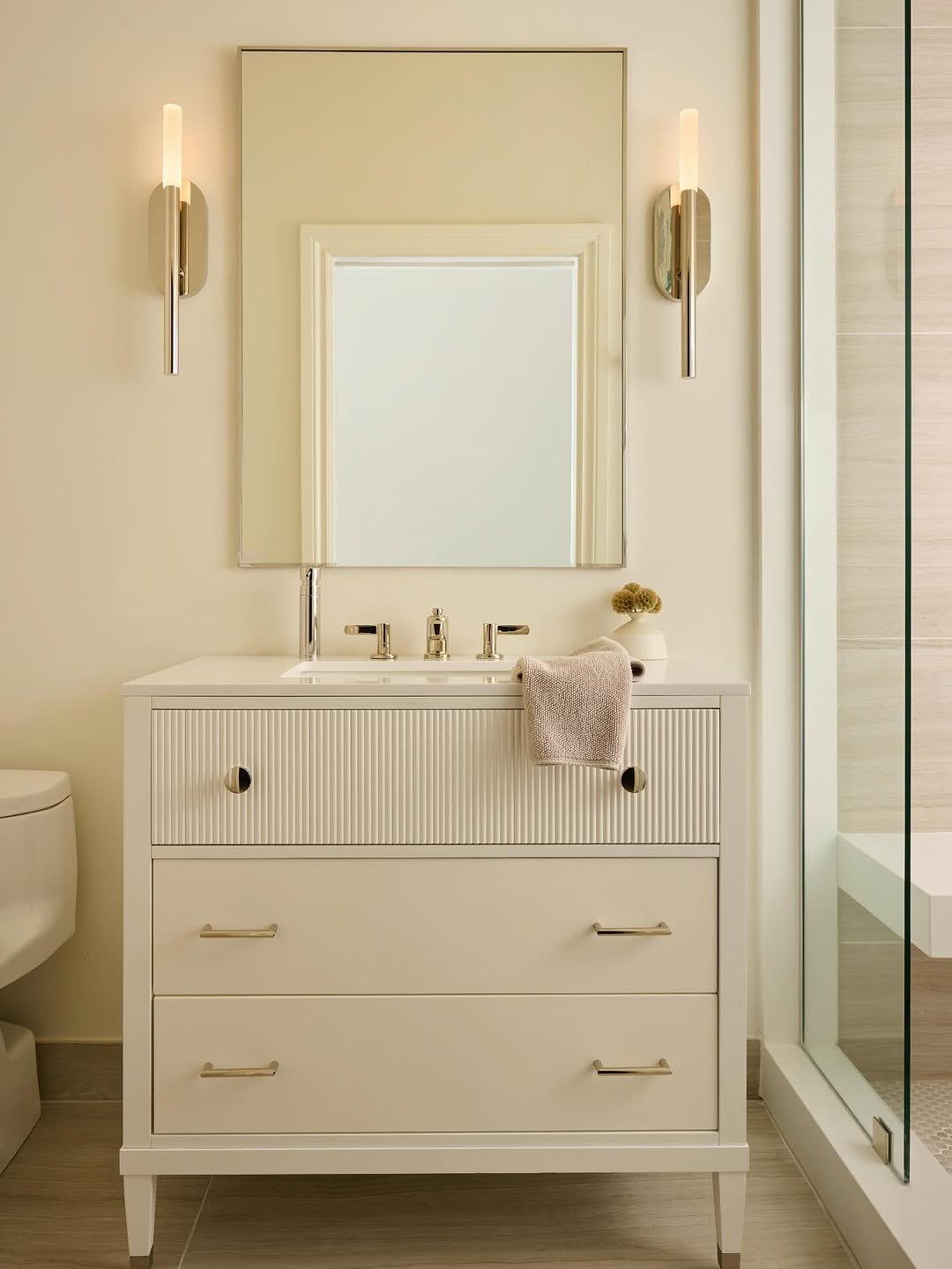 Bathroom with a fluted vanity, brass sconces and warm cream walls