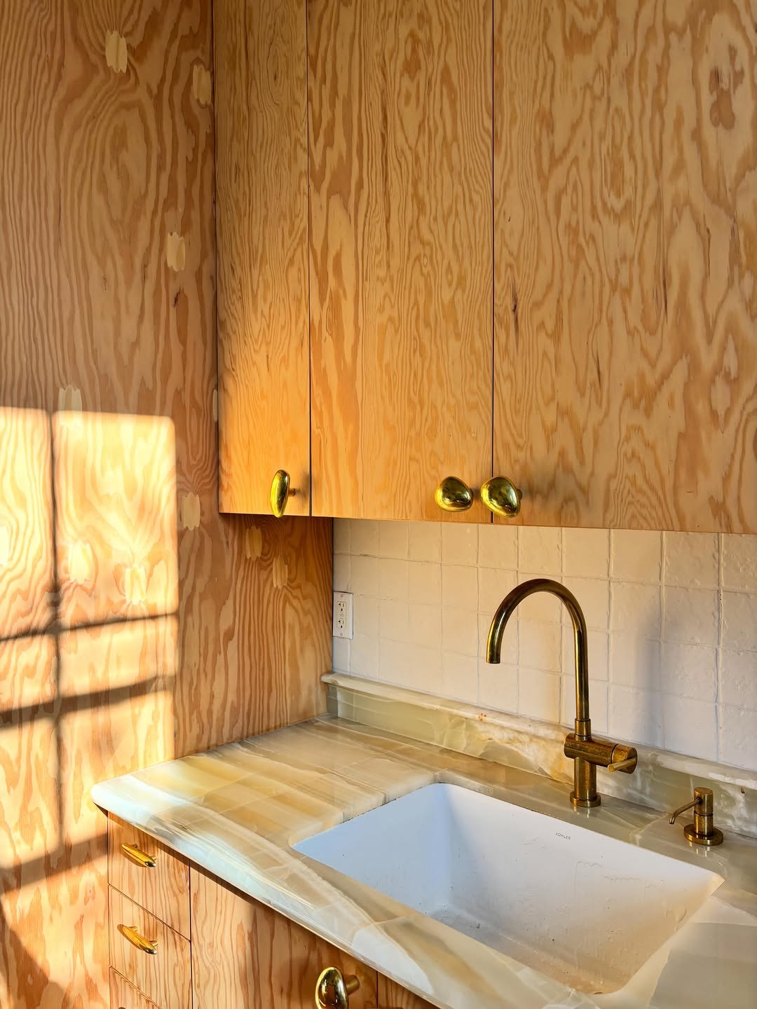 Kitchen with raw plywood cabinetry, brass hardware and a stone counter
